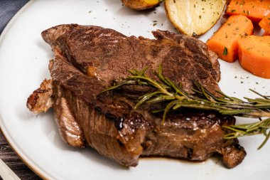 Biftek, ahşap bir masada patates ve havuçla servis edilir. Hava görüntüsü, 45 derece, yakın çekim.