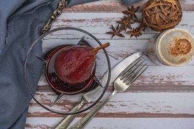 Kırsal alanda sunulan cam bir kasede sunulan kırmızı şaraplı armut, ahşap bir masada..