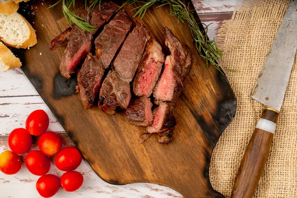 Churrasco of meat cut into pieces on a wooden board in a rustic setting.