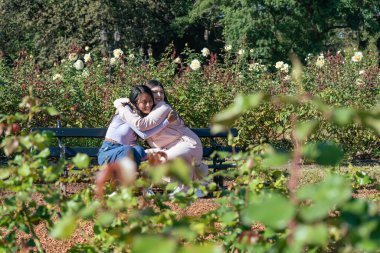 Parktaki bankta oturmuş mutlu bir şekilde sarılan iki genç kadın..