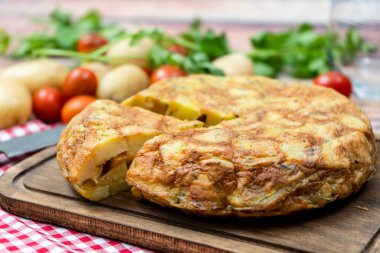 Normal bir İspanyol patatesi ya da patates omletinin kırsal bir ortamda patates ve çeri domatesli ayrı bir porsiyonu. Geleneksel İspanyol mutfağı. Seçici odak.