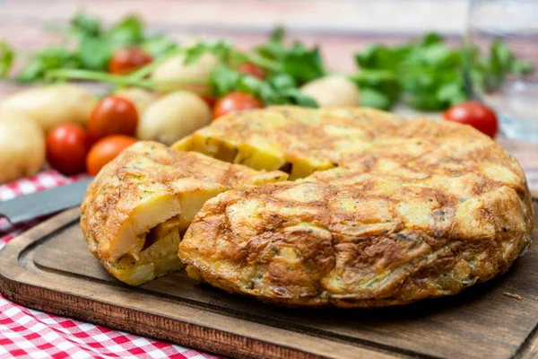Normal bir İspanyol patatesi ya da patates omletinin kırsal bir ortamda patates ve çeri domatesli ayrı bir porsiyonu. Geleneksel İspanyol mutfağı. Seçici odak.