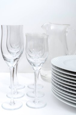 Yığılmış tabaklar, kristal kadehler ve beyaz bir masada cam sürahi..