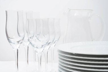 Yığılmış tabaklar, kristal kadehler ve beyaz bir masada cam sürahi..