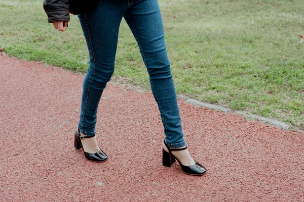 Woman\'s legs with shoes and pants walking on a path in a public park.