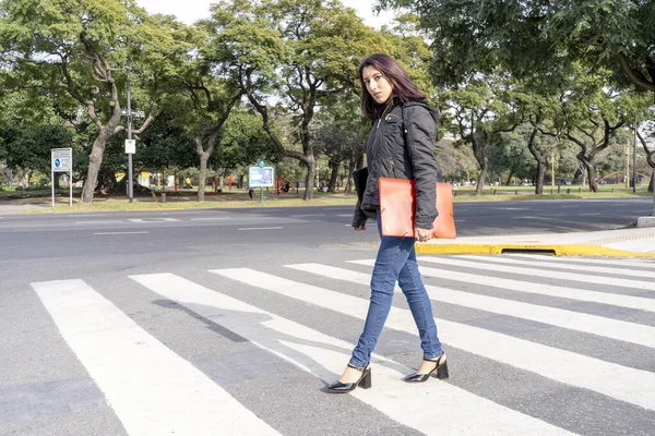 Young college woman in autumnal clothes crossing a street on the pedestrian path or zebra crossing. Road safety concept.