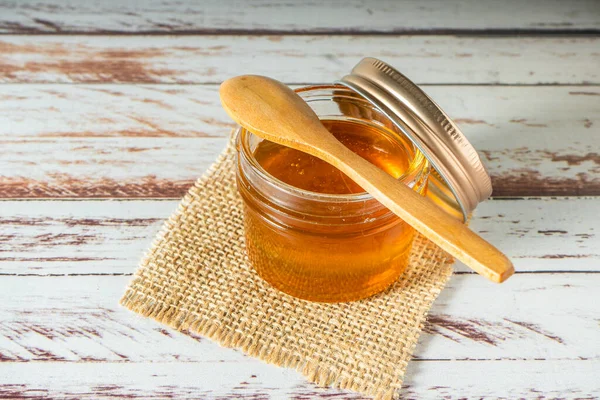 素朴なテーブルの上に小さな木製のスプーンで蜂からの純粋な蜂蜜の瓶 — ストック写真