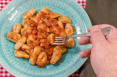 Lokanta çatalıyla birlikte açık mavi tabakta servis edilen domates soslu ev yapımı gnocchi alıyor. İtalyan yemeği..