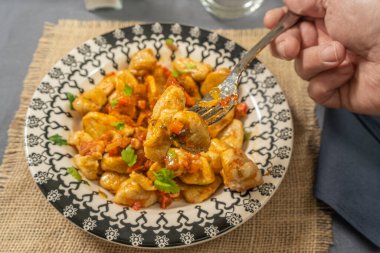 Lokanta çatalıyla birlikte açık mavi tabakta servis edilen domates soslu ev yapımı gnocchi alıyor. İtalyan yemeği..