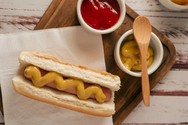 Ahşap bir tahtanın üzerinde hardallı, ketçaplı ve hardallı bir sosisli sandviçin üst görüntüsü. Fast food konsepti.