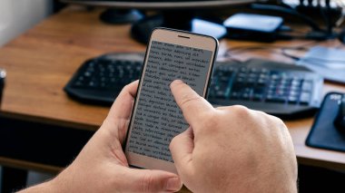 Ofisteki masasında çalışırken cep telefonundaki mesajın üzerinde işaret parmağını gezdiren bir adamın arkasından bak. Telekomünikasyon, bağlantı, 5G teknoloji kavramı.