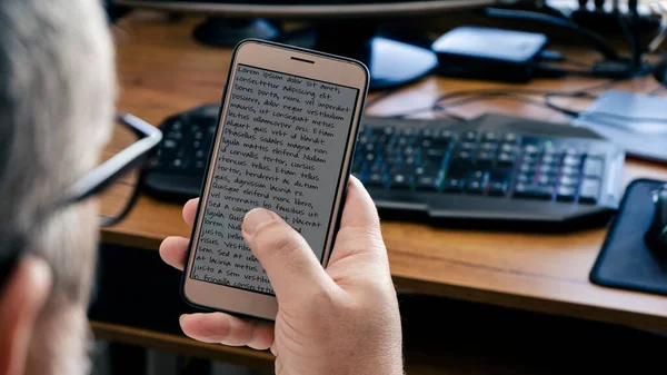 Ofisteki masasında çalışırken cep telefonuna bakan bir adamın arkasından bak. Telekomünikasyon, bağlantı konsepti.