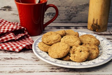 Kuru üzümlü yulaf ezmeli kurabiye, kırmızı kupa ve peçeteli klasik bir kır tabağı manzarası. Doğal beslenme kavramı.