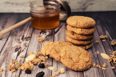Bir yığın ev yapımı yulaf ezmeli kurabiye içinde kuru üzüm, tohum ve arka planda bir kavanoz bal. Doğal ve organik beslenme kavramı.