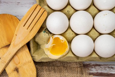 Kırsal ahşap bir tezgahta kırılan bir yumurtalı organik beyaz tavuk yumurtasıyla normal bir yumurta kutusu görüntüsü..