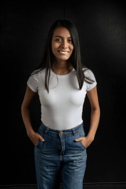 American shot of a beautiful smiling Latin woman with a white shirt and tame in her pockets on a black background. VErtical orientation