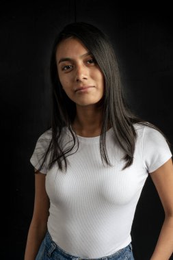 Medium short portrait of a beautiful smiling latin woman in white shirt on black background. Vertical orientation.