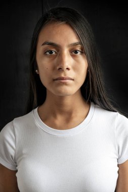 vertical medium close-up shot of a serious and beautiful black haired woman wearing a white T-shirt on a black background.