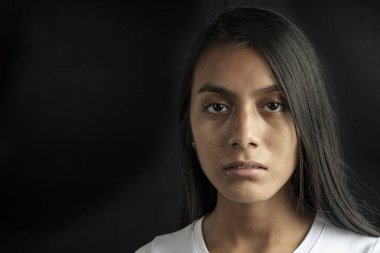 Close-up of a serious and beautiful black haired Latina woman wearing a white T-shirt on a black background. Copy space