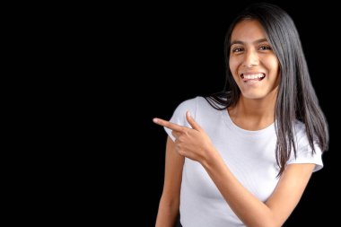 Beautiful latin woman with white t-shirt on black background pointing with her index finger and smiling looking straight ahead.