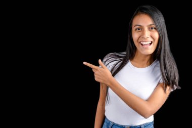 Beautiful Latin woman on a black background pointing with her index finger and smiling, looking at the indicated space.