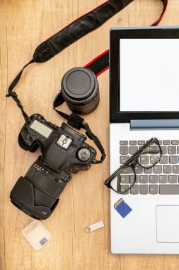 View of an open laptop with a reflex camera and a pair of glasses on the keyboard ready to work from home. Technology and communications concept.