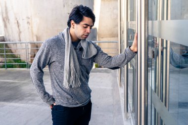 Çekici bir genç adam modern bir binanın cam kapısının kolunu tutuyor.