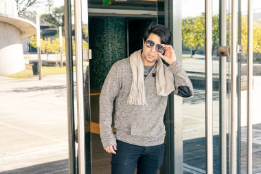 Çekici bir gencin aynalı duvarları olan bir binadan çıkarken orta boy fotoğrafı..