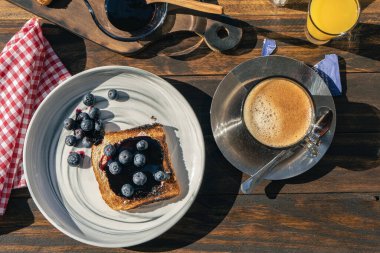 Taze yaban mersini ve böğürtlen reçeli ve sade kahveye eşlik eden zengin bir ekmeğin hava manzarası. Sağlıklı ve doğal kahvaltı kavramı.