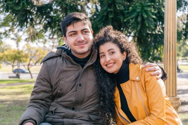 Genç çift parkta otururken adam kadına sarılıyor. Aşk konsepti.