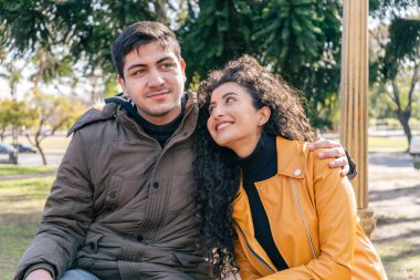 Genç çift parkta otururken adam kadına sarılıyor. Aşk konsepti.