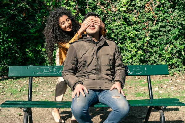 遊び心のあるカップル 彼女のパートナーの目を覆う美しい女性がベンチに座っている間 — ストック写真