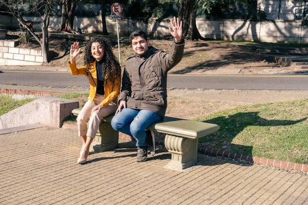 若いカップル一緒に公園に座って 遠くの人に手を振っ 友情の概念 — ストック写真