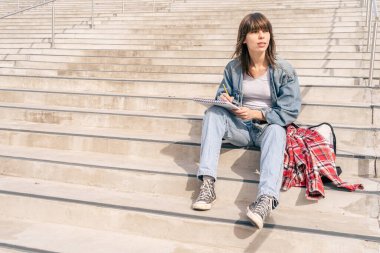 Elinde kalem çizimiyle merdivenlerde oturan bir kadın. Sanat ve ilham kavramı