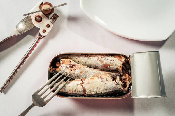 打开罐头的沙丁鱼油旁边的罐头开罐器 盘子和叉子上的白色大理石状表面 海洋食品产品 — 图库照片