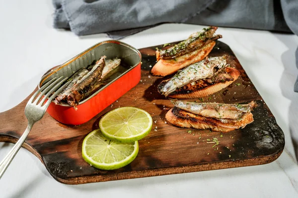 Arrangement of Spanish tapas of sardines in olive oil on toasts on a rustic wooden board and a can of sardines next to the tapas. High view.
