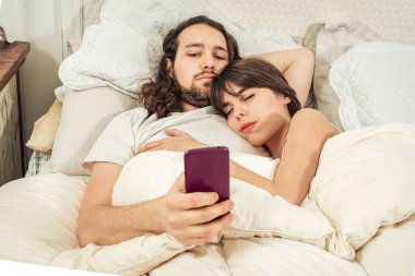 Mutlu çift yatakta yatan uyanma sonra cep telefonunuzda sohbet. Gülümseyen, mesaj, sosyal ağlar kontrol onun kız arkadaşı dostum. Çevrimiçi iletişim, mobil uygulamalar, internet üzerinden yemek siparişi