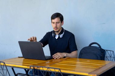 Dizüstü bilgisayarına odaklanan, bir kafede çalışan ya da çalışan boynunda kulaklıklarla modern çalışma kavramları sergileyen bir adam.