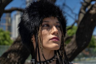 Siyah kürk şapkalı ve sivri uçlu boyunlu, güneşli bir günde geleceğe bakan kendinden emin genç bir kadın.