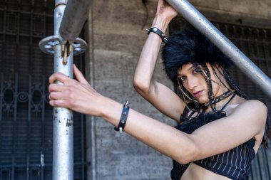 İskeleye karşı poz veren genç bir kadın, meydan okuyan bir şehir portresi yaratıyor ve alternatif modayı ifade ediyor.