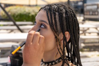 Profesyonel bir makyöz örgülü ve çivili yakalı bir kadına göz farı sürüyor. Alternatif bir bakış yaratıyor.