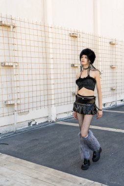 Alternatif gotik tarzda yürüyen genç bir kadın, kürk şapkası, eteği, mini eteği, file çorapları ve tüylü bacak ısıtıcıları var.