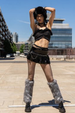 Kendine güvenen genç bir kadın, sahte kürk şapka, etek, mini etek, file çorap ve platform ayakkabısı giyerek kendine has bir şekilde poz veriyor.