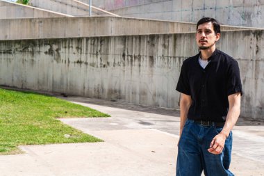 Genç adam çiğ beton barbar bir duvar boyunca tek başına yürüyor, düşünceli ve odaklı, şehir tarzı, modern şehir yalnızlığı.