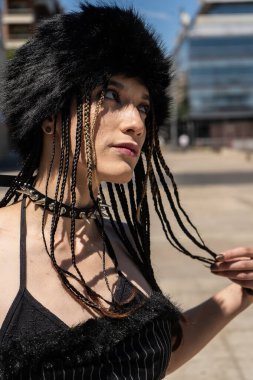 Örgülü saçları, sahte kürk şapkası ve çivili kolyesi olan, kenar mahalle modası ve kendine güvenen şehir tarzı portresi olan bir kadın.