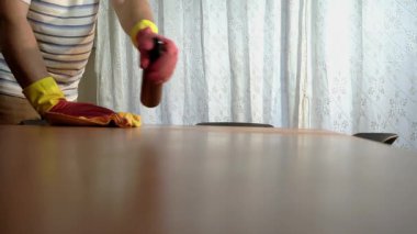 Koruyucu lastik eldivenli, gayretli bir hizmetçi titizlikle deterjan sıkar ve mikrofiber bezle ahşap bir masayı silerdi.