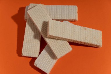 Turuncu arka planda duran waffle kurabiyeleri tatlı tatlılar ve çıtır çıtır atıştırmalıkları temsil ediyor. Yiyecek ve hamur işi kavramları