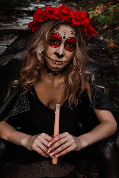 Joyeux Halloween concept. Horrible femme effrayée en tenue spéciale, porte un crâne d'argile blanche, un maquillage professionnel du crâne de sucre pour paraître effrayant, porte des vêtements noirs jouant avec une bougie — Photo