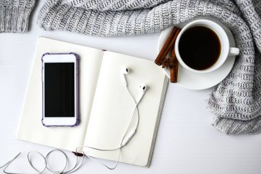 Not defteri kulaklıklı bir fincan kahve tarçın çubukları ve beyaz arka planda anason yıldızı. Etrafta süveter var. Kış sabahı rutini. Kahve molası. Uzayı kopyala Üst Manzara. Kahvaltıda. Düz yatıyordu