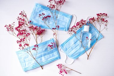 Yeniden kullanılabilir tekstil maskesi ve dezenfektan seçin. Beyaz arka planda pembe çiçekli yeniden kullanılabilir yüz maskesi. El yapımı tekstil maskesi. Coronavirüs salgını sırasında sıfır atık yaşam tarzı. Evde kalıp karantina altında kalmak.